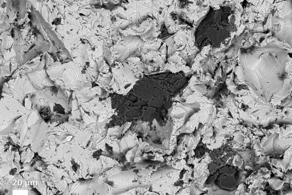 Scanning electron micrograph of a steel surface with sharp, angular features, 20 micrometre scale bar